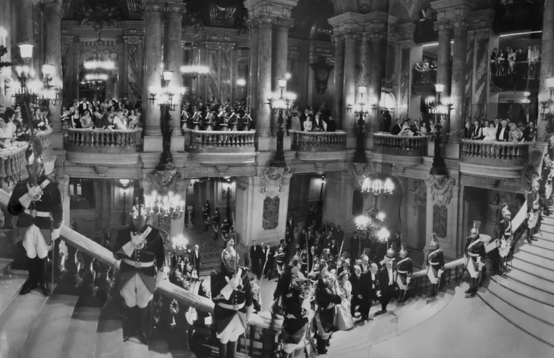 اگر چه بریتانیا همچنان مشکلات پس از جنگ را تحمل می کرد، برخی از مفسران تاج گذاری را به عنوان طلوع عصر جدید الیزابت توصیف کردند. در اینجا، الیزابت دوم ملکه انگلستان از پلکان بزرگ در اپرا در پاریس، فرانسه بالا می رود